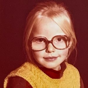 Anna-Elina Lyytikäinen alakouluikäisenä poolopaidassa, villaliivissä ja suurissa silmälaseissa.