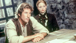 Kino: Sommersby. Richard Gere nojaa puiseen pöytään, Jodie Foster istuu takana.