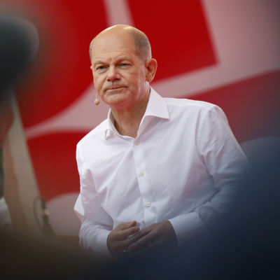 Olaf Scholz i en vit skjorta. Han tittar framåt.