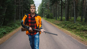 Ett vapen i huset inger respekt. Mannen spelas av Jon Henriksen En man kommer gående med jaktgevär på en sandväg.