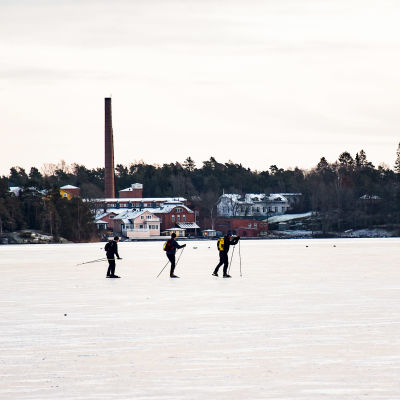 Tre personer åker skridsko på isen.