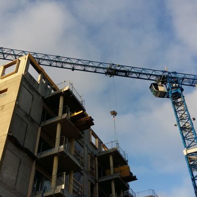 En blå lyftkran lyfter upp byggmaterial till ett flervåningshusbygge.