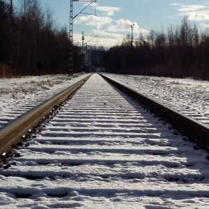 Ett tomt järnvägsspår en solig vinterdag med snö.