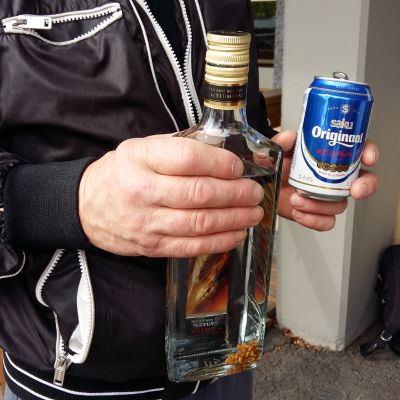 En man håller i en flaska starksprit och en burk öl.
