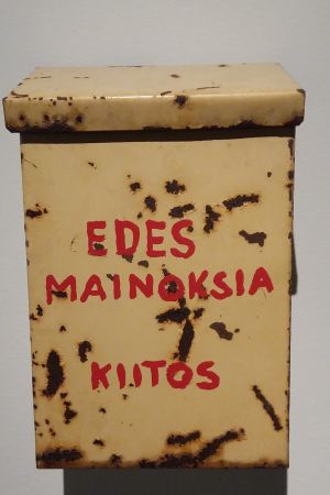 Ett konstverk signerat Kari Cavén. Kari Cavéns konstverk som föreställer en rostig brevlåda med texten "Edes mainoksia, kiitos" från år 2011.