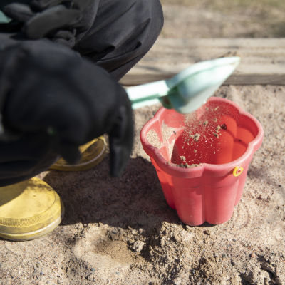 Ett barn häller sand i en hink i sandlådan.