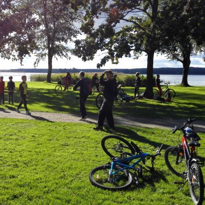 En park där det går och cyklar flera barn som spelar Pokémon Go.