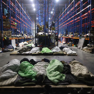 Migranter sover på rad i en lagerlokal.