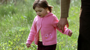Tyttö kävelee niityllä aikuisen kanssa.