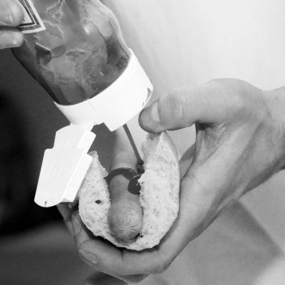 Svartvit bild på hand som håller i hotdog och ketchupflaska.