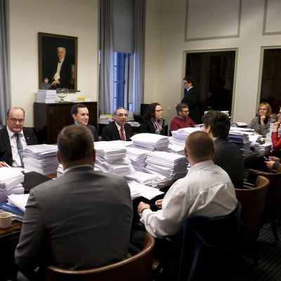 Grundlagsutskottet sitter samlat vid ett långt bord fullt med pappershögar.