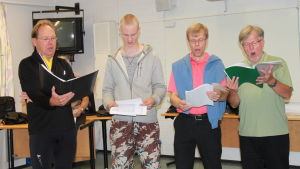 Neljä miestä vilkaisee nuotteja oopperaharjoituksissa.