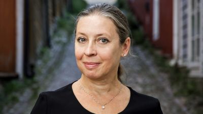 Medelålders kvinna poserar i en gränd med äldre trähus.
