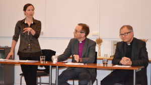 Julia Korkman, här tillsammans med biskop Björn Vikström och Roger Rönnberg, kyrkoherde i Esbo. Korkman har lett flere utredningar om sexuella övergrepp. Julia Korkman, Björn Vikström och Roger Rönnberg vid ett podium.