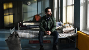 Khaled (Sherwan Haji) sitter på en säng i en flyktingscentral och ser ut genom fönstret.