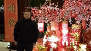 Christoffer Norrgård har inte ändrat sina rutiner på grund av coronaviruset. En man klädd i svart poserar framför en röd banderoll med kinesiska tecken. Mannen står brevid en ljusinstallation av kinesiska lampor och körsbärsträd