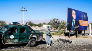 En afghansk säkerhetsvakt granskar området invid platsen där en bomb dödade minst 24 personer den 17 september i staden Charikar. Bomben var riktad mot sittande presidenten Ashraf Ghanis valmöte. Affishen till vänster är en valaffish med Amrullah Saleh, som ställer upp som vicepresidentkandidat. En säkerhetsvakt granskar området i närheten av platsen där en bilmbomb detonerade i staden Charikar den 17. september 2019.