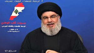 Hassan Nasrallah höll även han ett tv-sänt tal under fredagen. Man med skägg sitter framför blå vägg och håller tv-sänt tal.