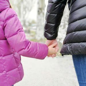 En flicka och kvinna går hand i hand. Flickan iklädd rosa jacka och kvinnan svart jacka.