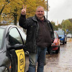 Amatörskådespelare, journalist och politiker. Jan-Erik Berglund hoppas på seger som obunden kandidat. Jan-Erik Berglund gör segertecknet framför bil med kandidatreklam i regnigt Mariehamn