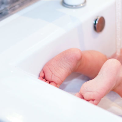 Litet barn får baken tvättad i tvättställ.
