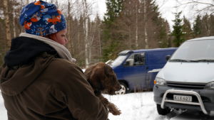 Riikka Simola kantaa mäyräkoiraa autoon metsästyreissulla.