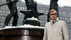 Michael Caine seisoo Kolmen sepän patsaan edessä. Kuva elokuvasta Miljardin dolalrin aivot.