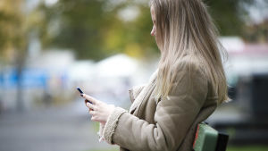 Sociala medier är på gott och ont. Under pandemin har unga lätt kunnat hålla kontakt med varandra men samtidigt kan de också skapa stor press på hur de unga ska vara. Ung kvinna sitter på en bänk med mobiltelefon i handen,