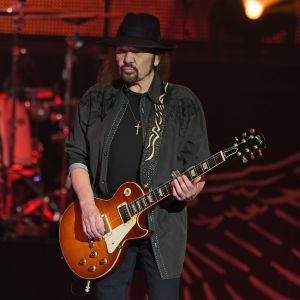 En man med långt svart hår och svart hatt spelar gitarr.