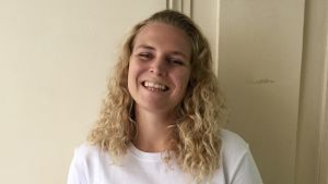 Erica har alltid känt en dragning till Paris och har pluggat franska sedan högstadiet. En kvinna med blont lockigt hår, står framför en vit vägg och skrattar.