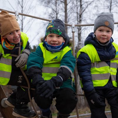 Kolme poikaa istuu kiipeilytelineessä esikoulun pihalla.