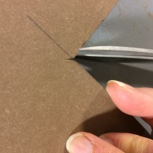 Leikkaa pienet viillot keskikohtaa kohti helpottaaksesi korin kulmien ompelemista. Sormet, paperinahka ja kulma joka leikataan.
