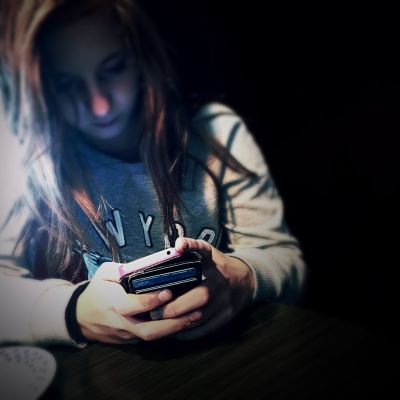 en tonårstjej tittar på sin mobiltelefon i mörkret