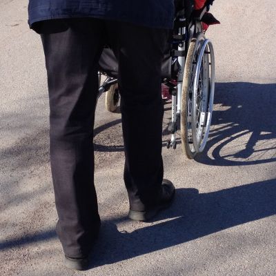 Person skuffar en person i rullstol.