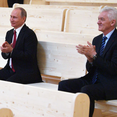 Vladimir Putin och Gennadij Timtjenko sitter bredvid varandra och applåderar.