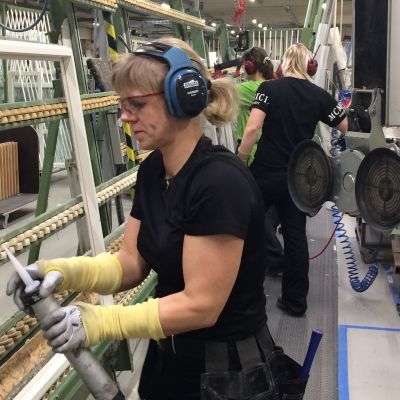 Suojalasit päässään oleva nainen työskentelee ikkunapuitteiden äärellä.