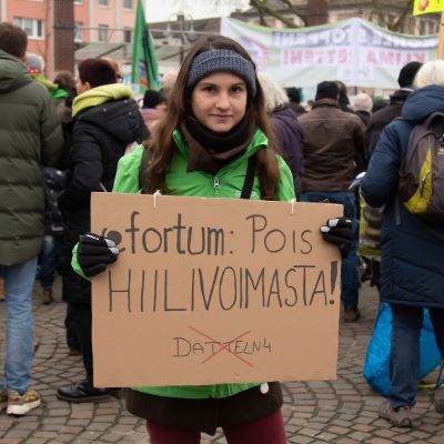 nainen kyltin kanssa, kyltissä lukee: "Fortum: pois hiilivoimasta!"