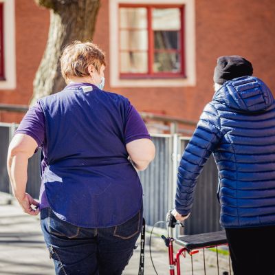 Vanhus rollaattorin kanssa hoitajan kanssa ulkoilemassa.