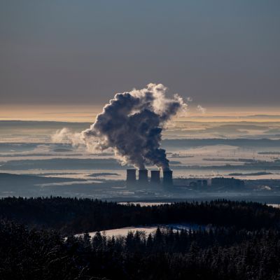 Hiilivoimala kuvattuna ylhäältä, piiput tupruttavat savua pilvien yli.