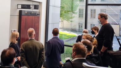 Den åtalade står utanför rättssalen omringad av media.