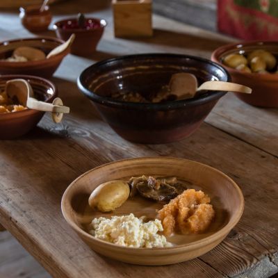 Pöydässä ruokaa, jota olisi tarjottu 1800-luvun puolivälin kievarissa; perunoita, possunpaistia, naurissosetta.