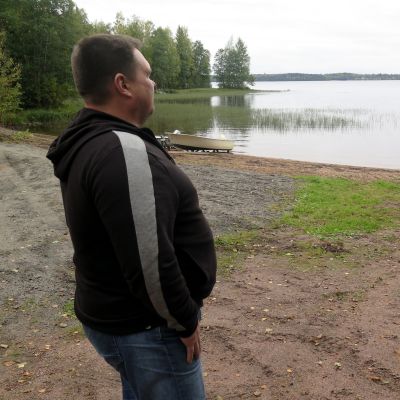 Mies seisoo rannalla ja katselee järven yli vastarannalle.