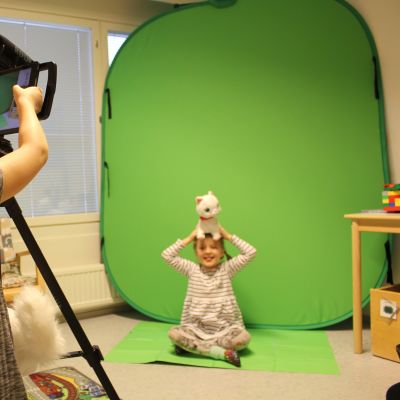 Päiväkotilapset kuvaavat toisiaan tabletilla green screen-kankaan edessä.