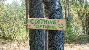 Kyltti jossa englanniksi teksti Clothing Optional eli suomeksi vaatetus vapaaehtoinen Natural High Healing Festivaalilla.
