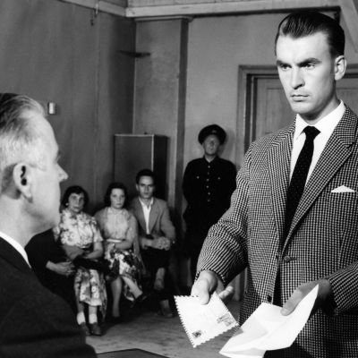 Komisario Susikoski (Ismo Kallio) esittelee todistuskappaletta oikeuden puheenjohtajalle (Aarne Välimäki) elokuvassa Kolmas laukaus (1959)