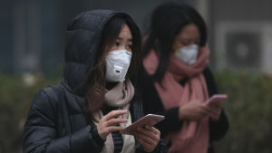 Många kineser lider av luftföroreningarna. Två kinesiska kvinnor skriver på sina mobiltelefoner i utsläppsröken i Peking den 20 december 2016.