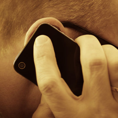 En närbild på en man som talar i en mobiltelefon. Mobilen och mannens hand täcker hans öra. 