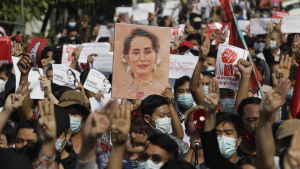 Demonstranterna kräver att deras ledare Aung San Suu Kyi släpps fri. En folkmassa demonstrerar med plakat och med uppsträckta händer. De bär munskydd.