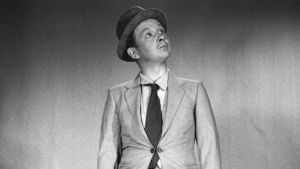 Pöysti i filmen Syndabocken från år 1957. Lasse Pöysto seisoo suorana mustavalkoisessa kuvassa. Hänellä on kädessään matkalaukku ja hän katsoo hieman yläviistoon.