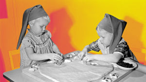 Kuvassa on kaksi lasta tonttulakit päässä leipomassa vuonna 1958